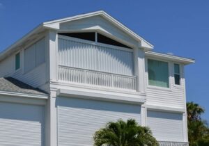 Large white home with roll-down and accordion style hurricane shutters protecting windows