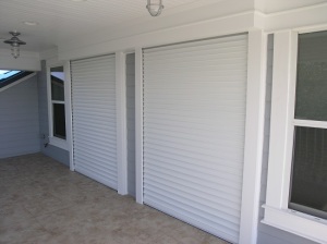 Grey residential property with two roll-down shutters closed over windows.