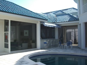 Retractable window screens installed on a yellow home with a dark roof.